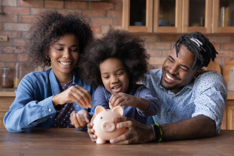 Pai e mãe negros sorridentes ajudam a filha a colocar moedas em um cofre de porquinho.