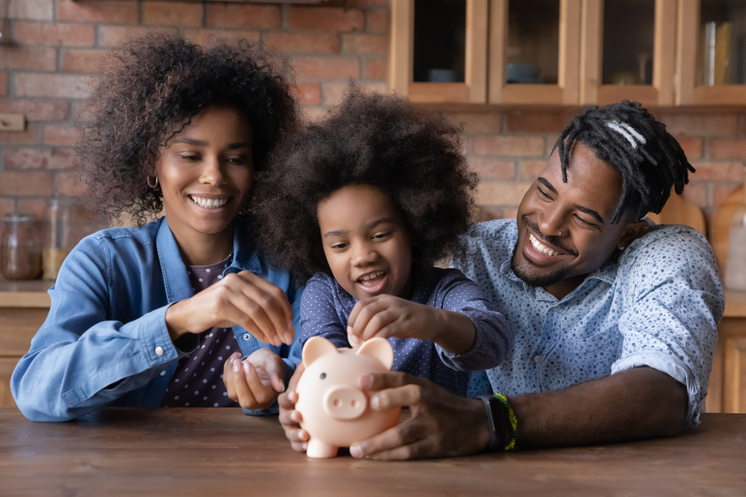 Pai e mãe negros sorridentes ajudam a filha a colocar moedas em um cofre de porquinho.