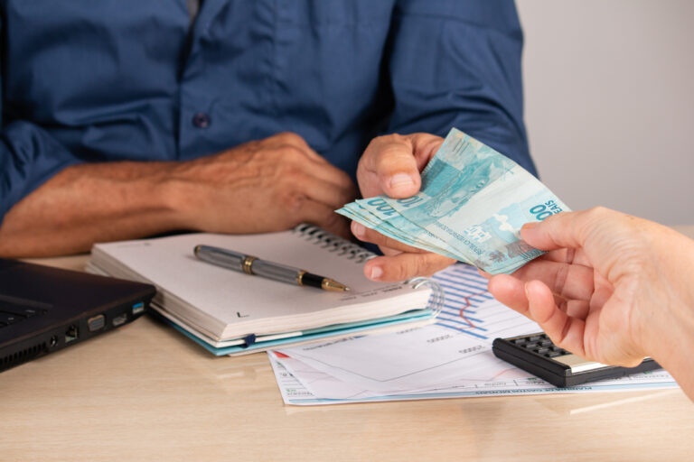 Uma pessoa recebe notas de cem reais de outra.