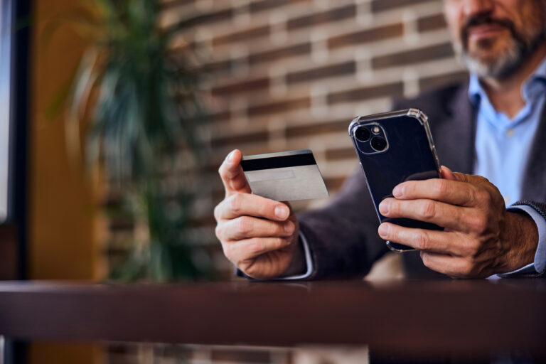 homem segura cartão de crédito e celular em mãos.